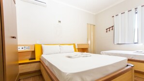 Habitación de hotel con dos camas, cabeceros de madera, una mesita de noche, aire acondicionado instalado en la pared y una ventana con cortinas.