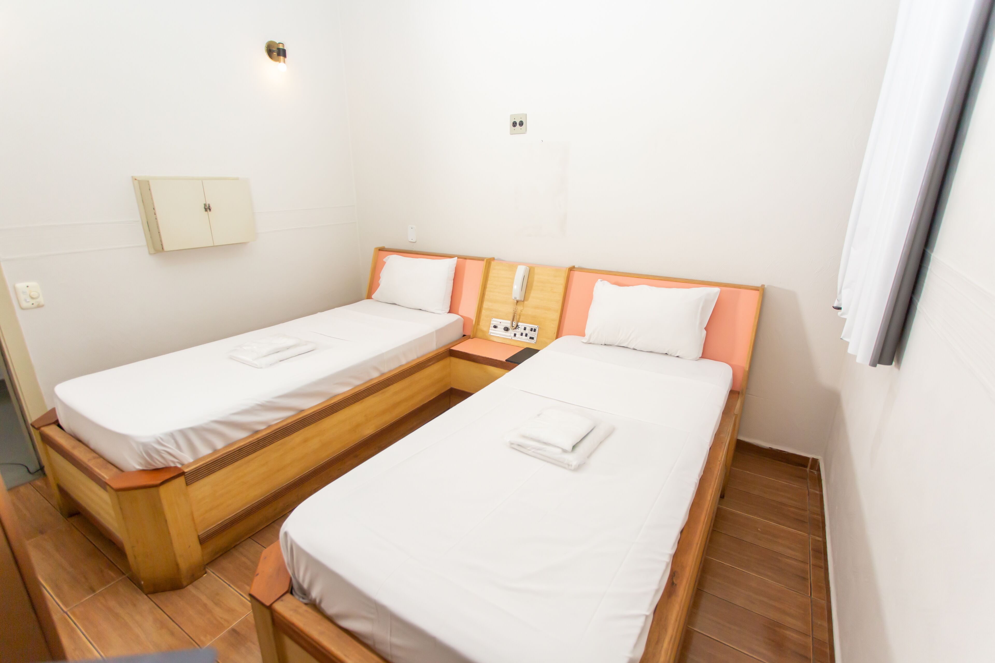 A small, clean room with two single beds, a wooden nightstand, a bedside telephone, and a small cabinet.