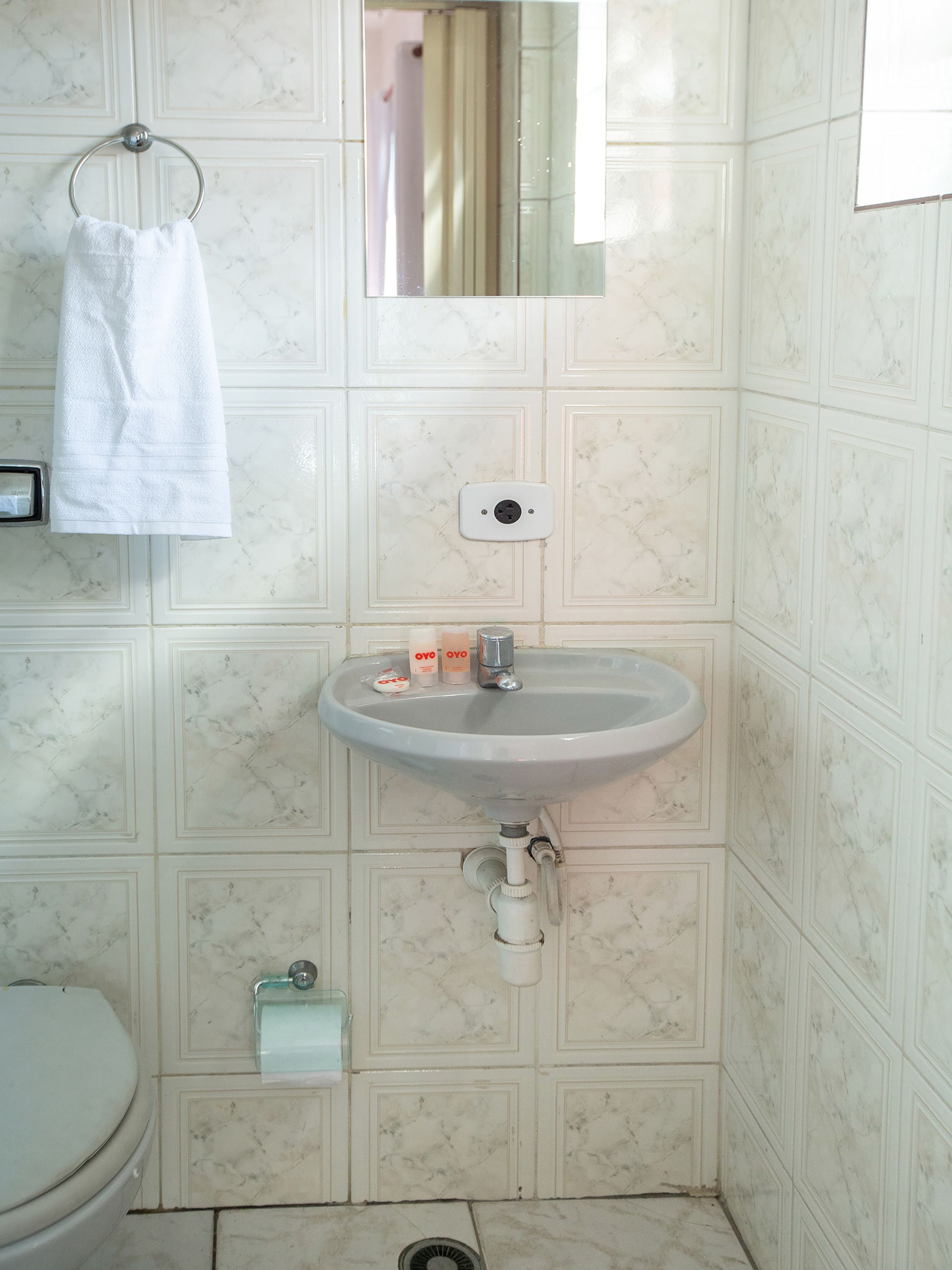 A bathroom with a white sink, a towel hanging on a metal ring, a mirror above the sink, and a toilet with a paper towel dispenser.