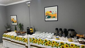 Una mesa de buffet con mantel de girasoles, cafeteras y diferentes tipos de comida.