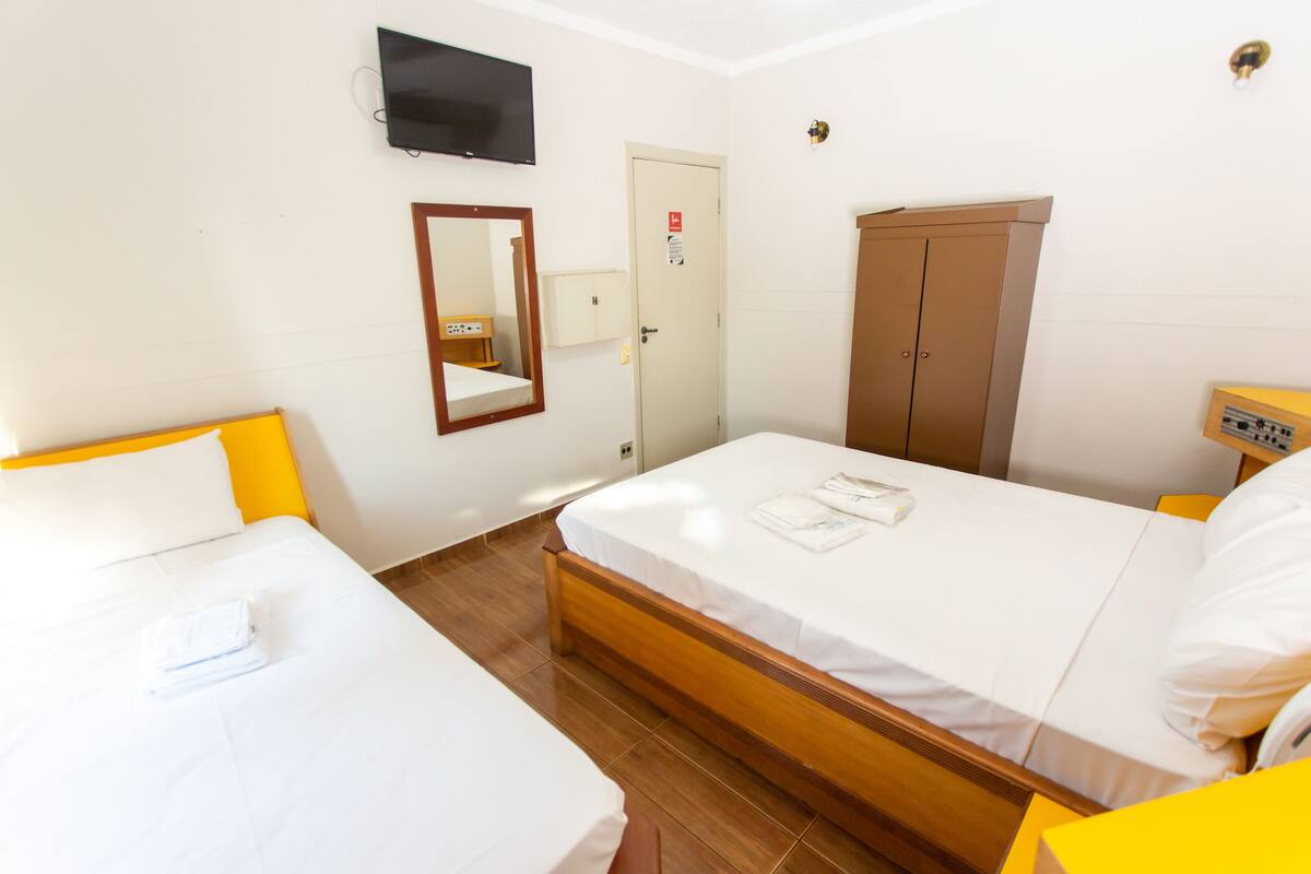 Een hotelkamer met twee eenpersoonsbedden, een aan de muur bevestigde televisie, een kledingkast en een deur met een veiligheidsbordje.