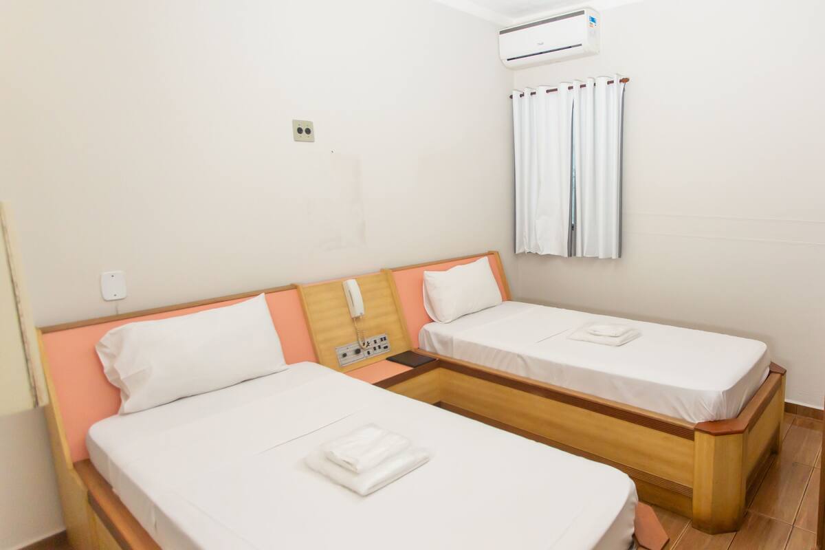 Hotelkamer met twee enkele bedden, een bedtelefoon, een airconditioning en een raam met gordijnen.