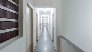 Un largo pasillo estrecho con paredes blancas y suelo gris, que conduce a varias puertas.