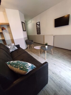 A modern living room with a dark sofa, a small round table, and a flat-screen TV mounted on the wall. - Le Nid du Pont de Gau (Saintes-Maries-de-la-Mer)