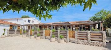 Un patio con un edificio blanco, cercas de madera y plantas en macetas.