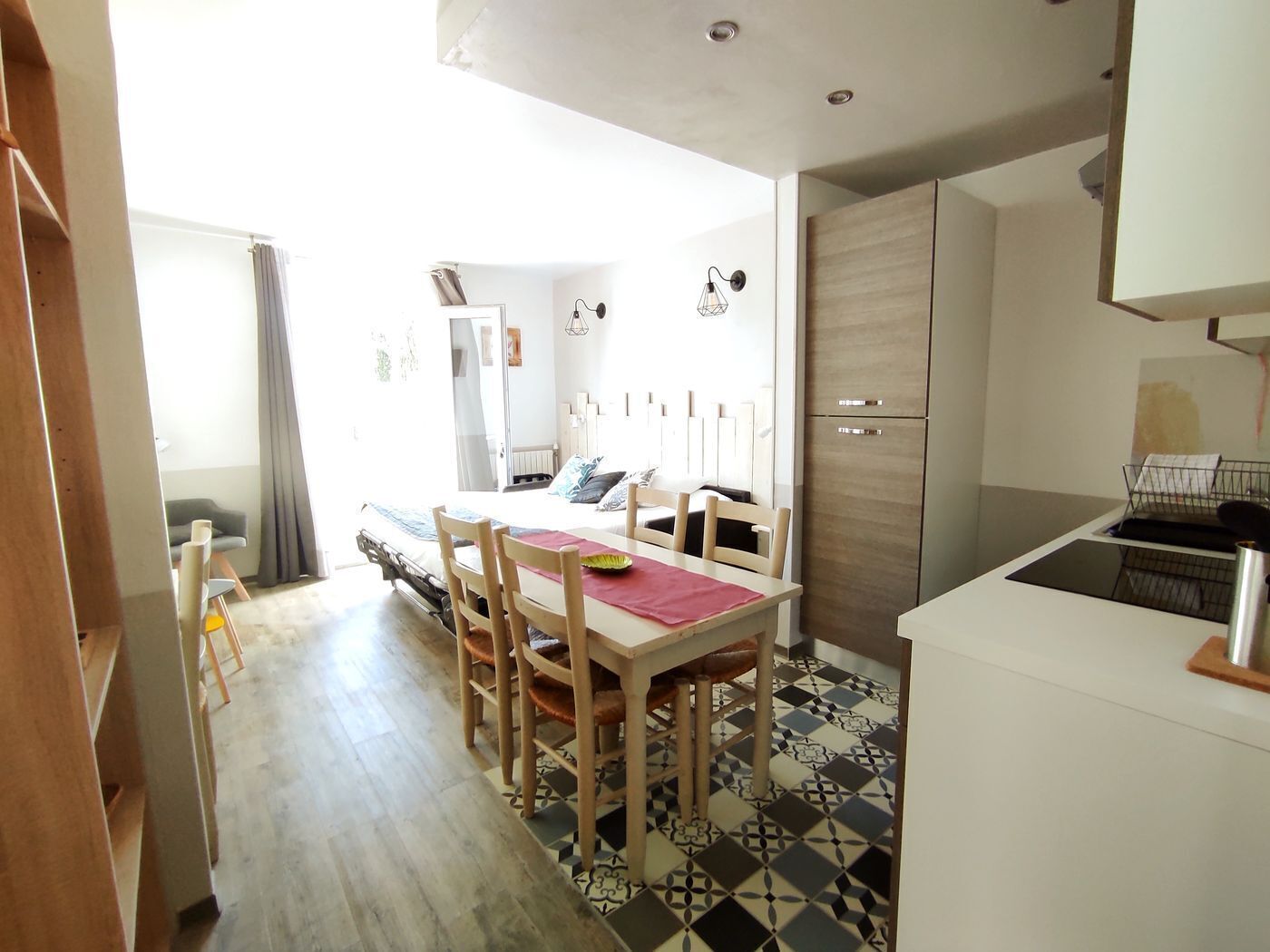 A compact kitchen with a dining area, featuring a checkered floor, wooden chairs, and a small table.