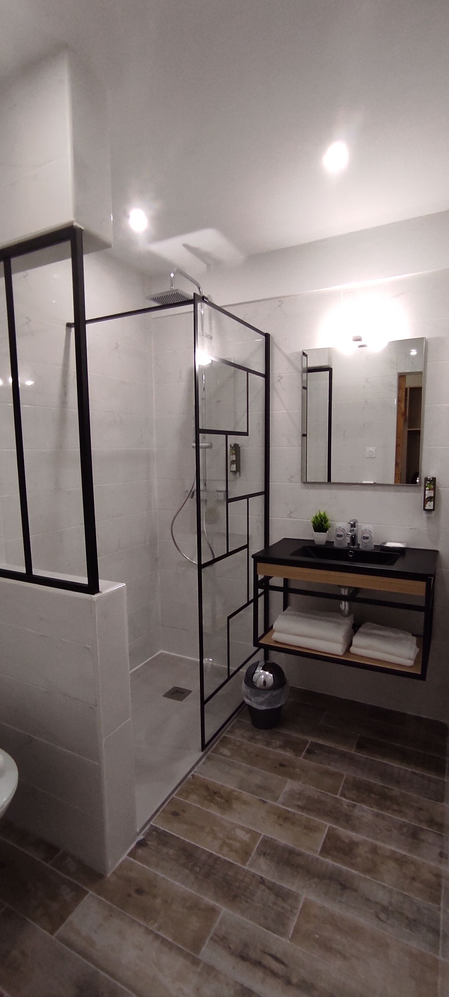 Un baño moderno con ducha de vidrio, un lavabo negro sobre encimera de madera y un espejo encima del lavabo.