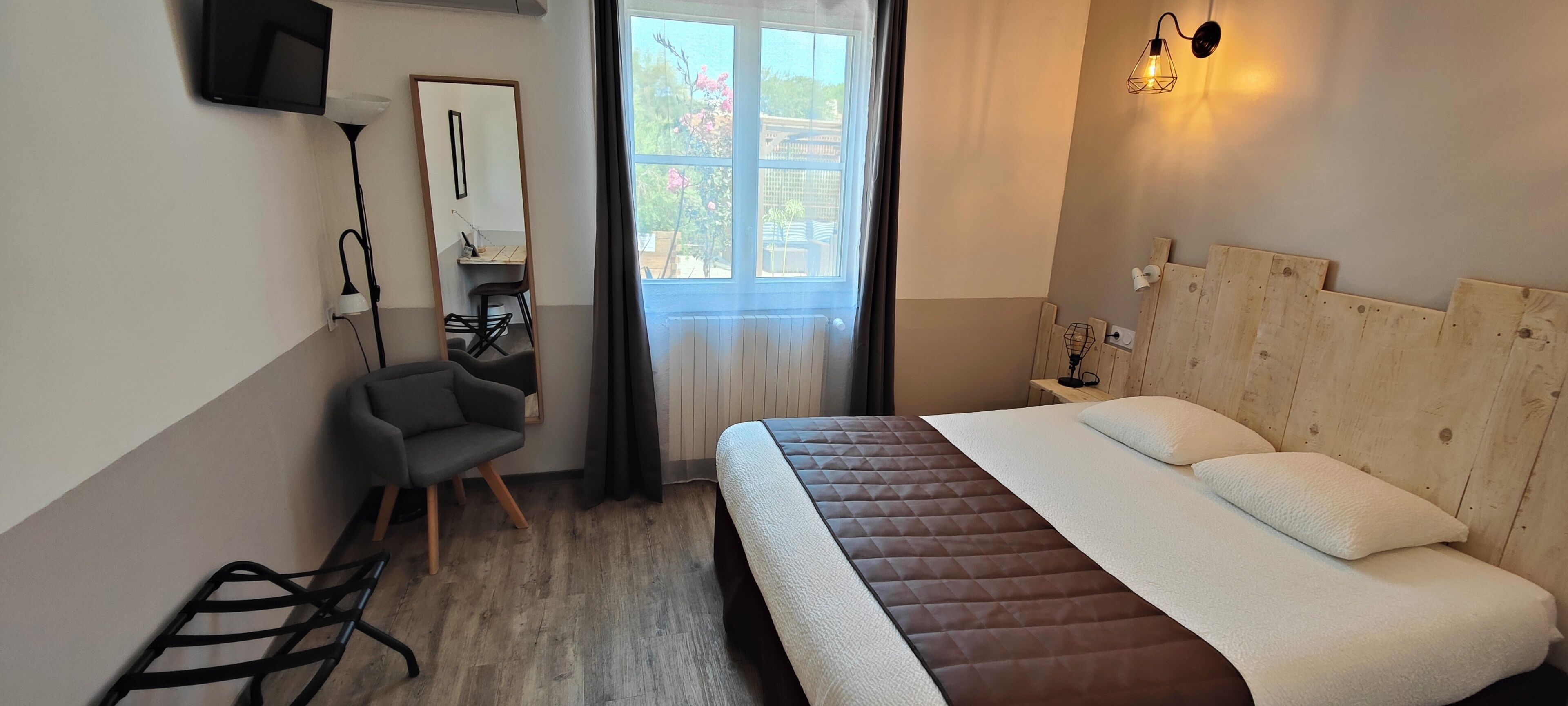 A bedroom with a bed, a desk, a chair, a TV, and a window with curtains.
