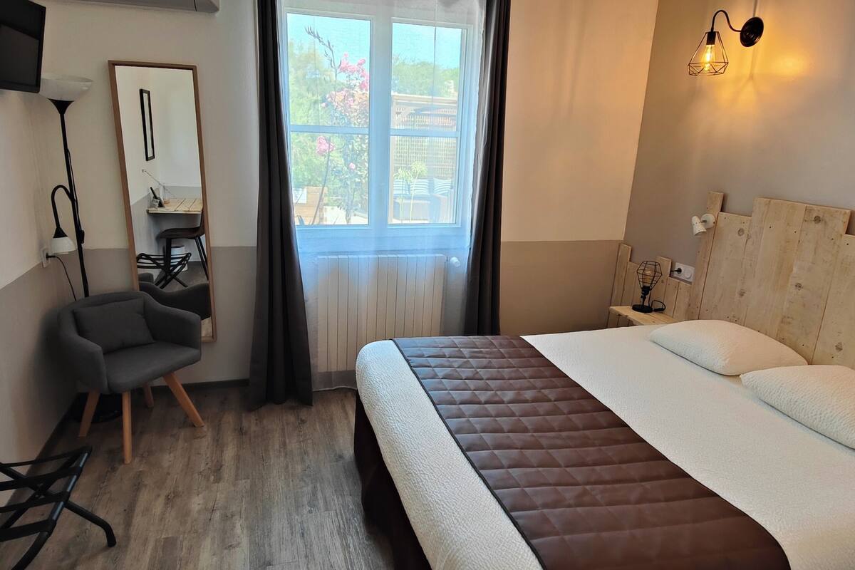 A bedroom with a bed, a desk, a chair, a TV, and a window with curtains.