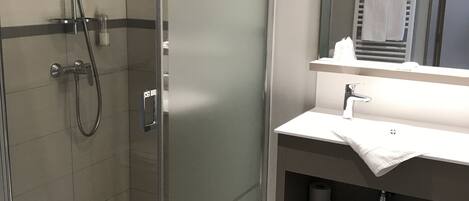 A modern bathroom with a glass-enclosed shower, a vanity with a mirror, and a towel rack.