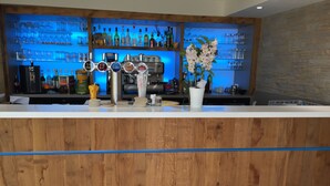 Angolo bar con un bancone in legno, diversi erogatori per bevande e un'ampia selezione di bottiglie e bicchieri sugli scaffali.