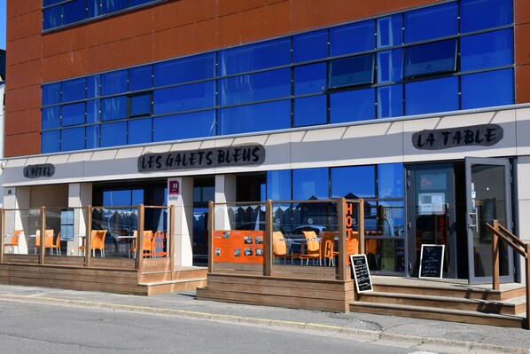 Un bâtiment moderne qui abrite un restaurant appelé « LES GALETS BLEUS » et un autre appelé « LA TABLE », tous deux situés au rez-de-chaussée.