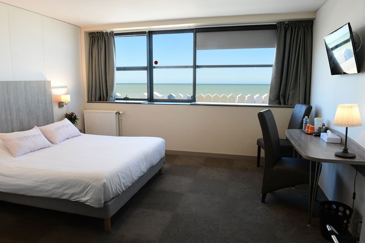 Habitación de hotel con cama, escritorio, silla, televisor y ventana con vista al mar.