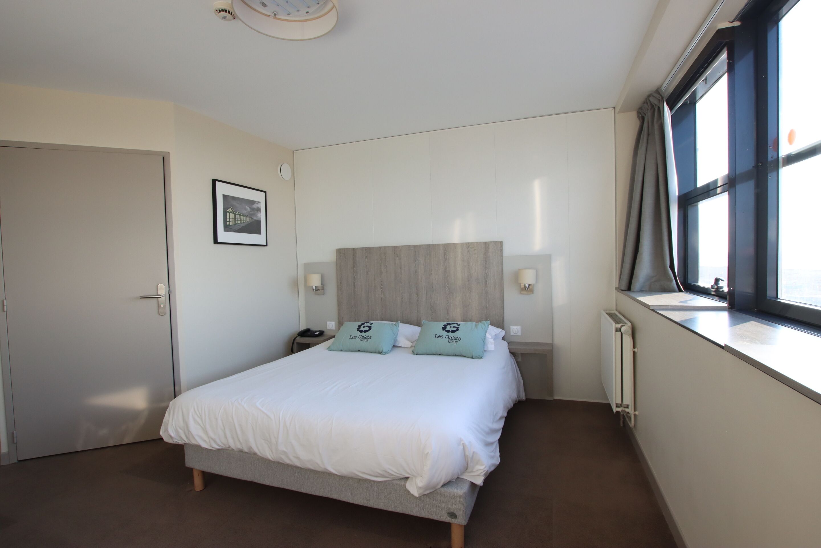 A bedroom with a bed, a nightstand, a framed picture on the wall, and a window with curtains.