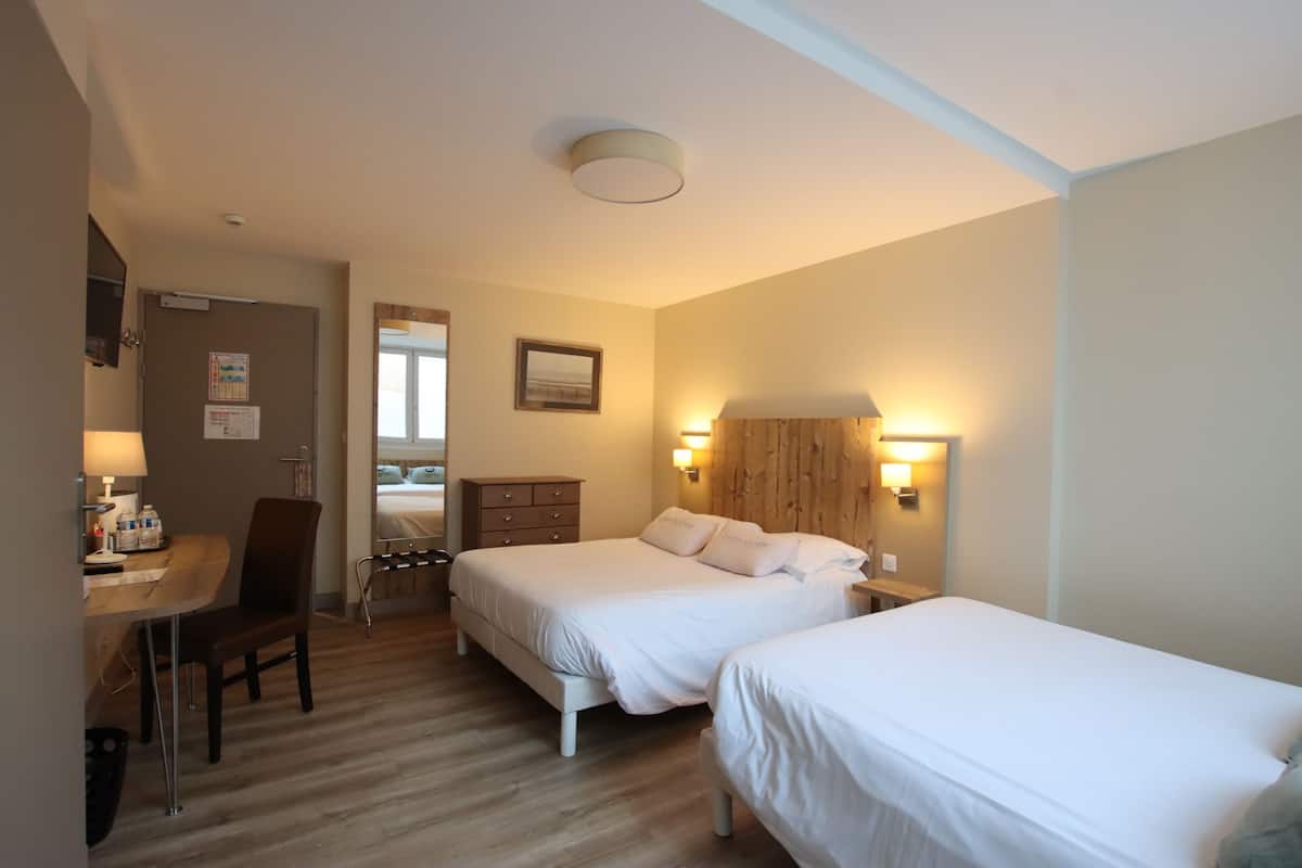 Habitación de hotel con dos camas, un escritorio, una silla y un aparador de madera.