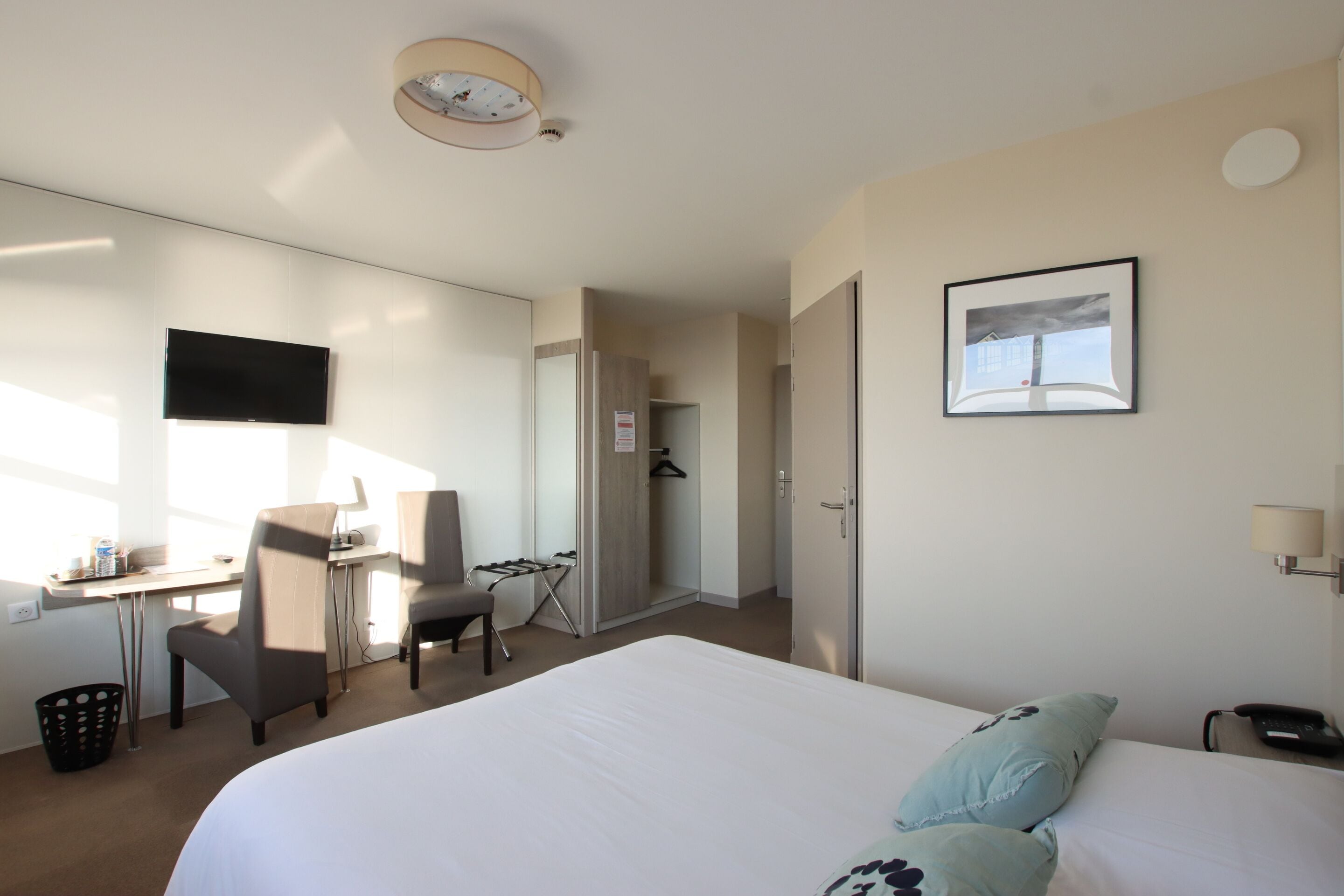 Habitación de hotel con una cama grande, un escritorio con silla, un televisor en la pared y un marco de fotos.