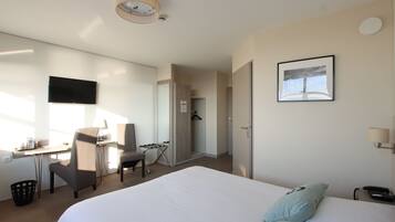 A hotel room with a large bed, a desk with a chair, a TV mounted on the wall, and a picture frame.