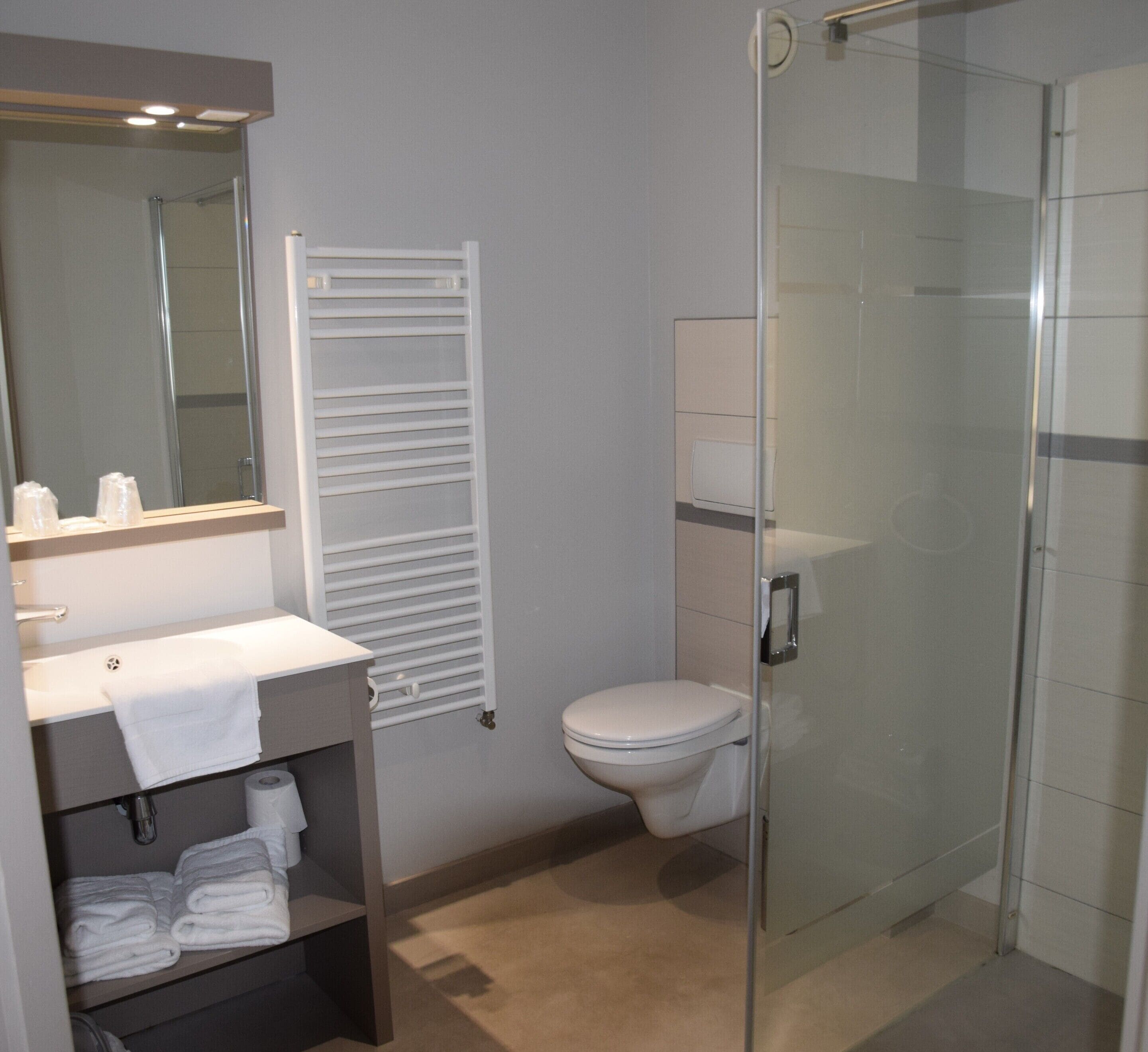 A modern bathroom with a glass shower enclosure, a white toilet, and a sink with a towel rack.