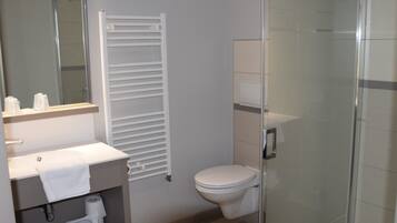 A modern bathroom with a glass shower enclosure, a white toilet, and a sink with a towel rack.