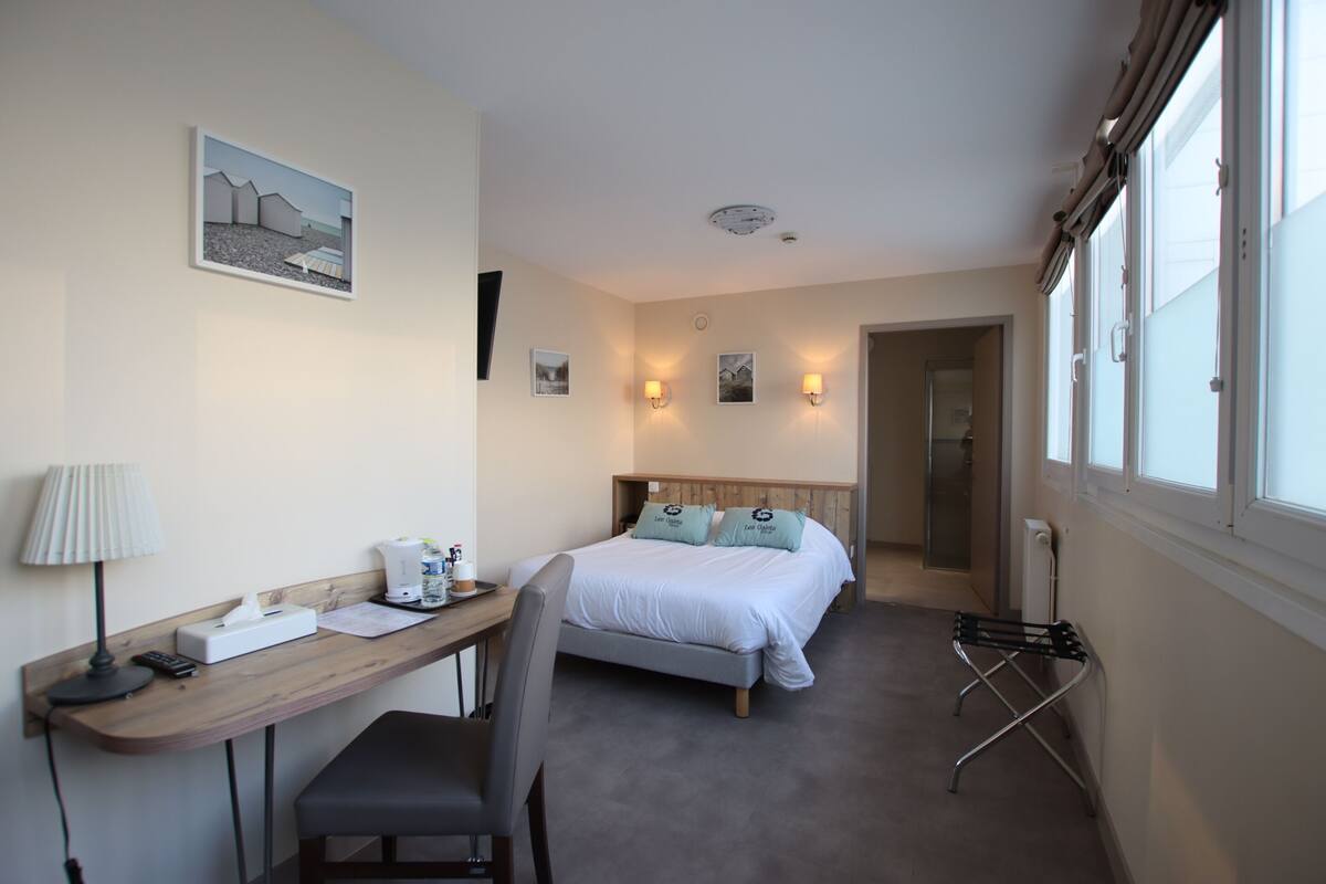 Habitación de hotel con cama, escritorio, silla, lámpara y vista al exterior.