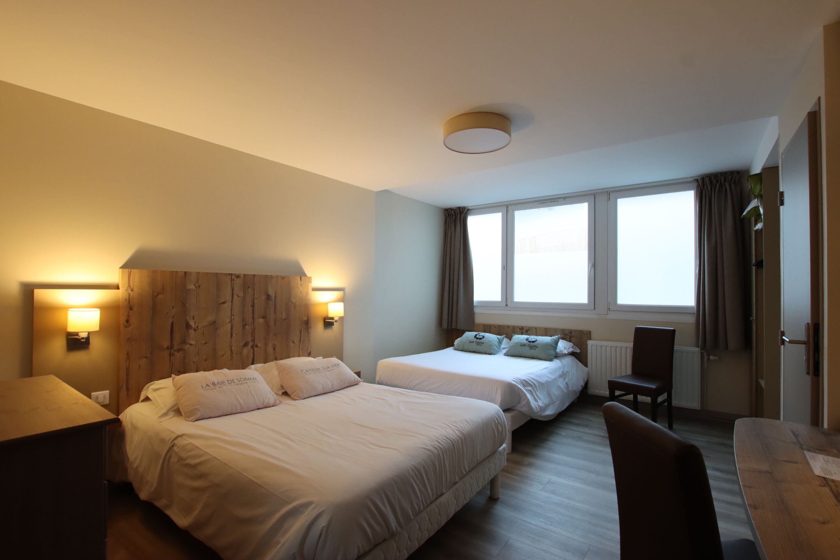 A hotel room with two beds, a wooden headboard, a desk, and a chair.