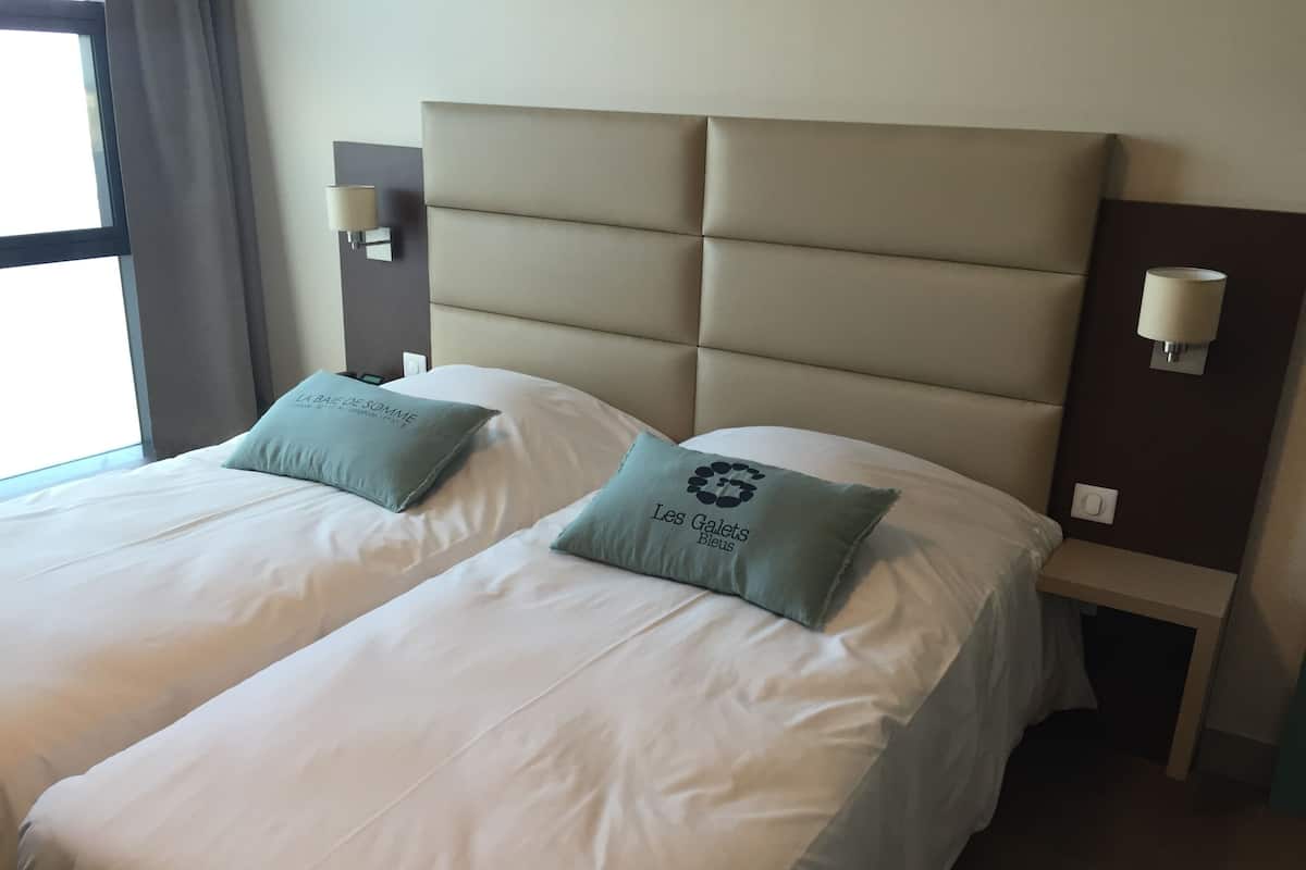Habitación de hotel con dos camas, cada una con una almohada y una mesita de noche con lámpara.