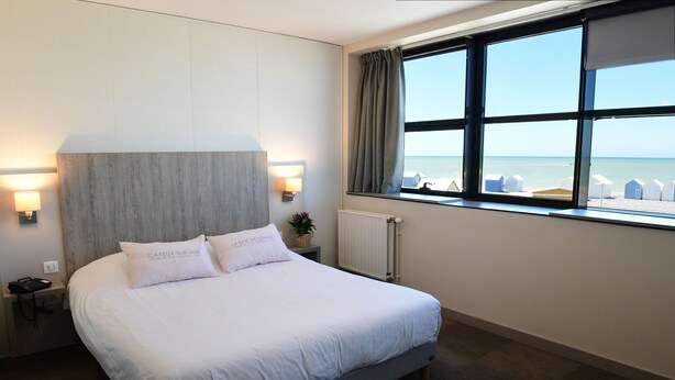 Camera d'albergo con un letto grande, vista sul mare e una finestra con ombrelloni sulla spiaggia.