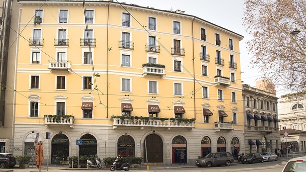 Um edifício amarelo com várias varandas e lojas, incluindo um restaurante e uma farmácia visíveis.