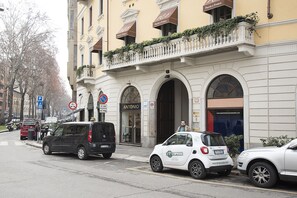 A street view with a building featuring a storefront labeled "ANTONIO" and a small white car parked in front.
