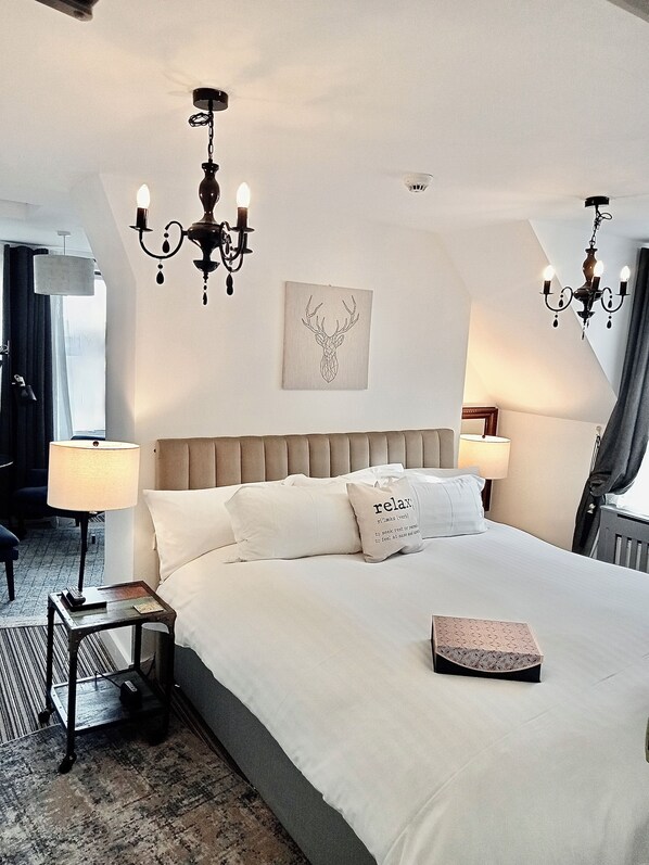 Habitación de hotel con una cama grande, dos lámparas de noche, un candelabro, una luz de techo y una obra de arte enmarcada en la pared.