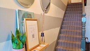 A staircase with striped carpet, a wooden console table with a framed picture, a potted plant, and a mirror. - Regency Rooms (Littlehampton)