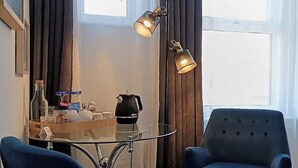 A room with two blue armchairs, a small table with a kettle and glasses, and a floor lamp. - Regency Rooms (Littlehampton)