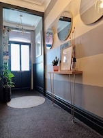 Um corredor com uma porta, um espelho redondo, uma pequena mesa com uma planta e um lustre.