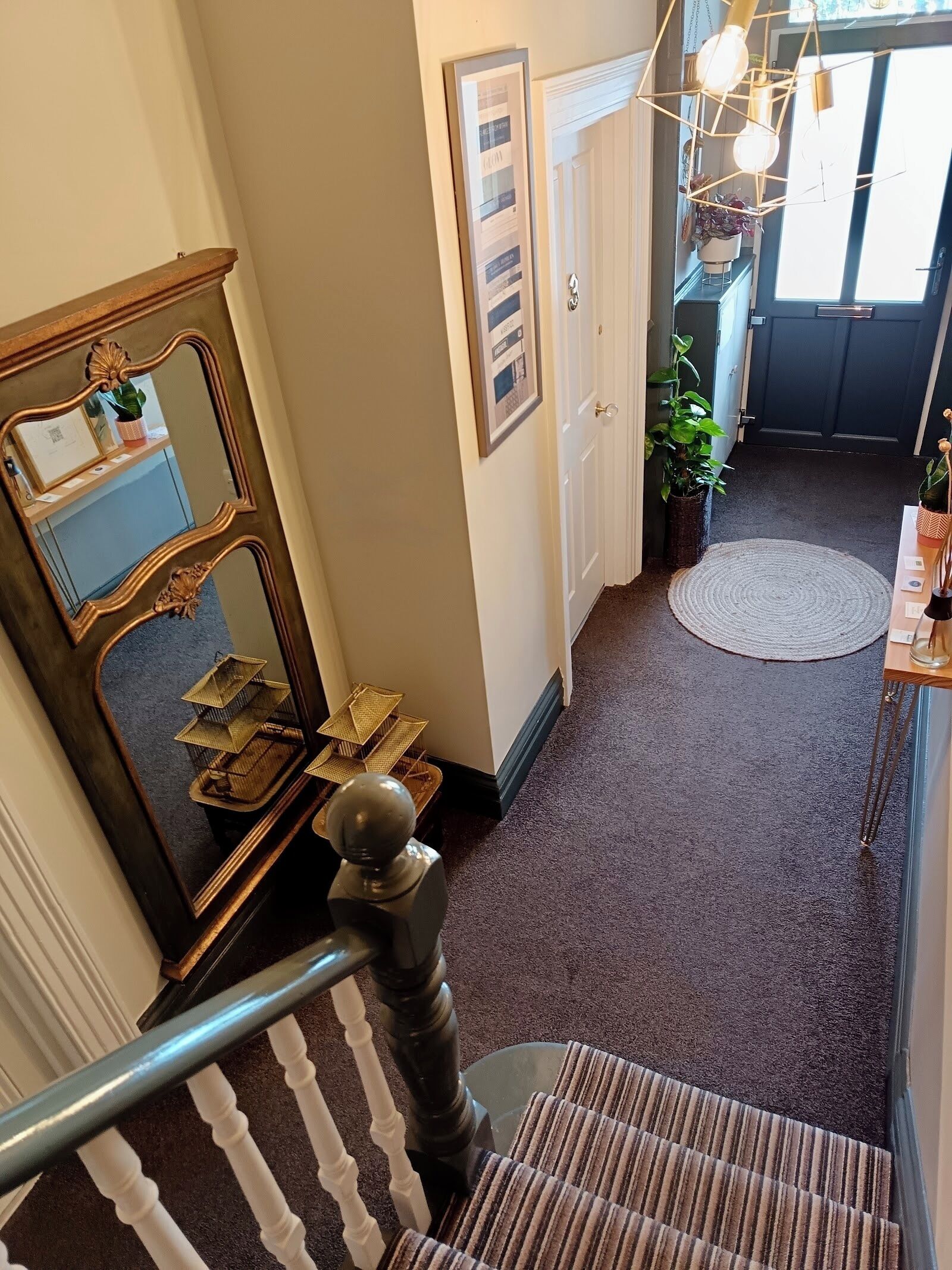 A staircase with a striped carpet, a wooden railing, a mirror, and a framed picture on the wall.