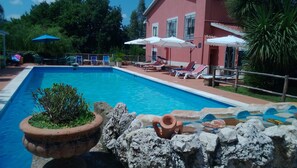 Ein Swimmingpool mit Liegestühlen und Sonnenschirmen, umgeben von einem roten Gebäude und Grünflächen.