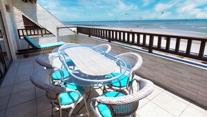Terraza con mesa y sillas, con vistas a una playa donde hay gente y cometas.