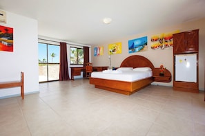 A hotel room with a large bed, a desk, a chair, a wardrobe, and a refrigerator. - Cumbuco Ocean View (Caucaia)