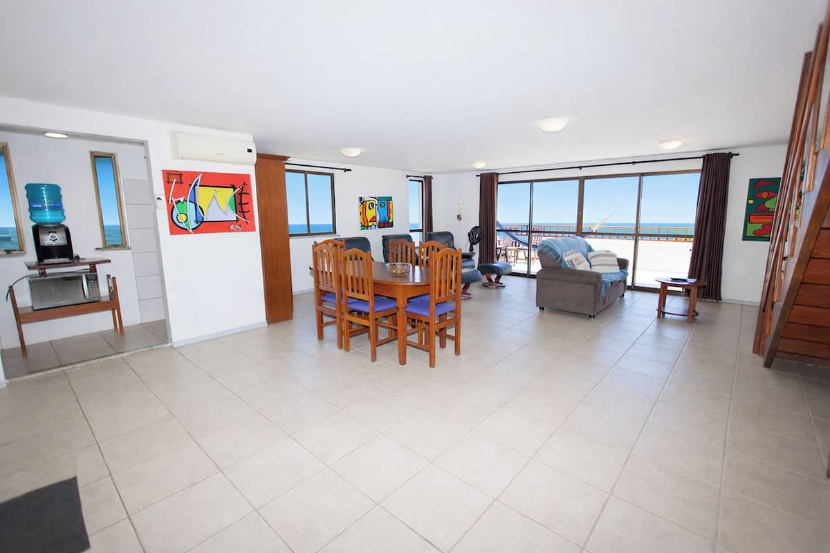 A spacious living area with a dining table and chairs, a sofa, and a view of the sea through large windows.