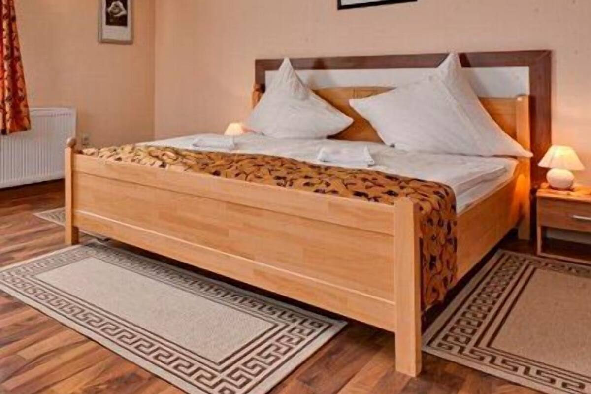 Een net opgemaakt bed met een houten hoofdbord, een bedlampje en een ingelijst schilderij aan de muur.