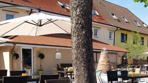 An outdoor seating area with wicker chairs and tables, a tree, and a building with a tiled roof in the background. - Hotel Restaurant Zum Ochsen (Bietigheim)