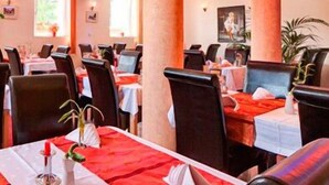 A restaurant with multiple tables, each with a red tablecloth and white napkins. The room has a modern design with large pillars and a ceiling with recessed lighting. - Hotel Restaurant Zum Ochsen (Bietigheim)