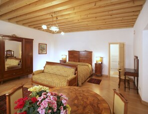 A bedroom with a wooden ceiling, a bed, a nightstand, a desk, and a chair. - Villa Busta Hotel (Montebelluna)