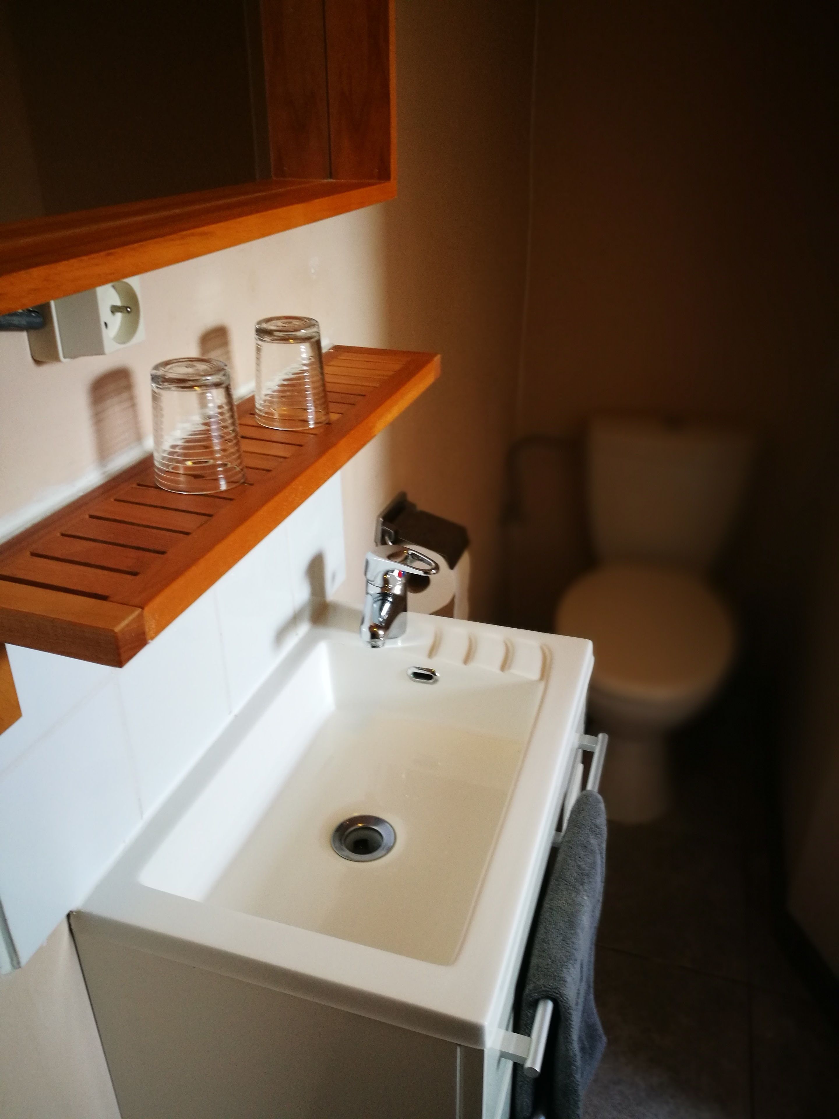 Un baño con lavamanos blanco, estante de madera y un inodoro.