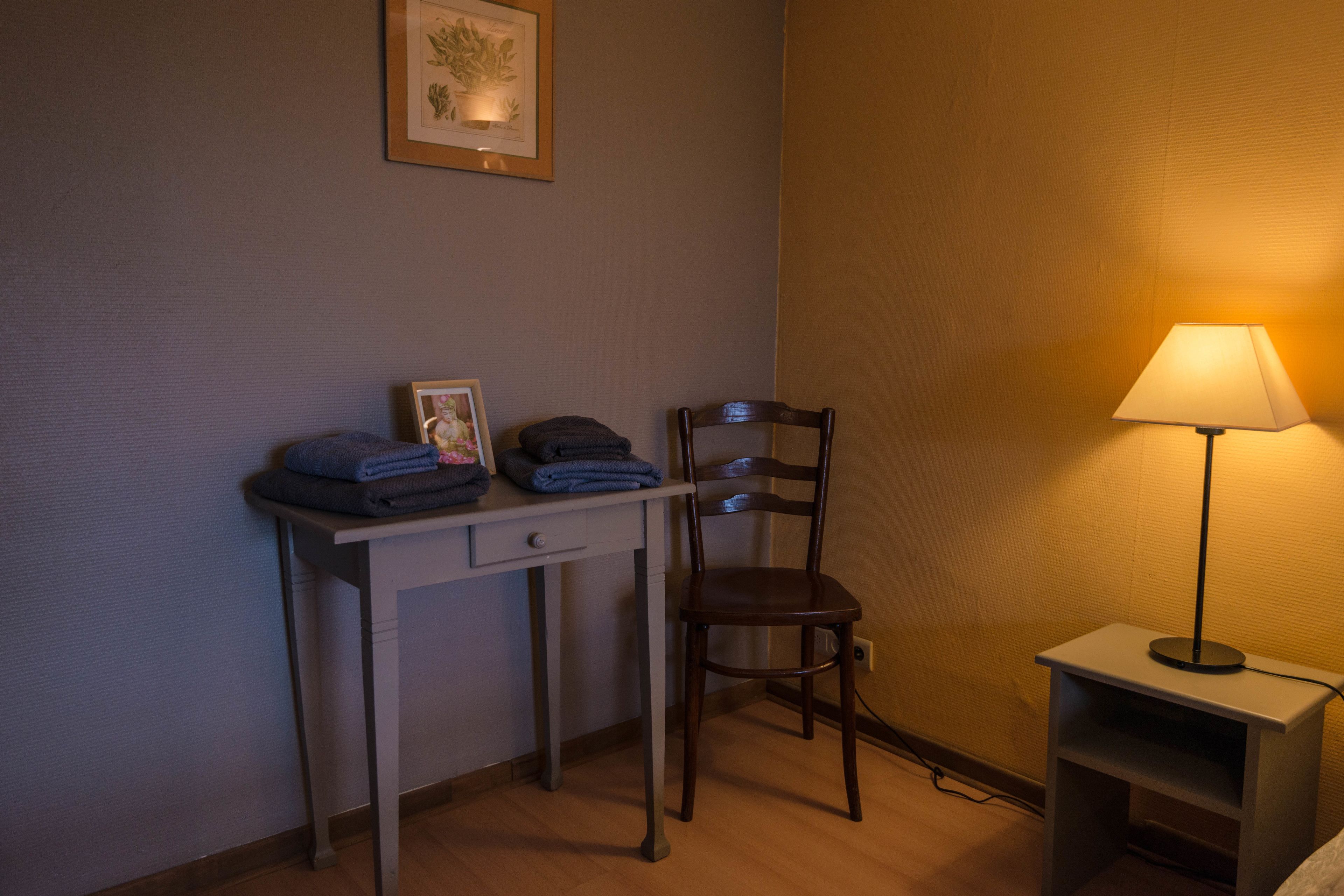Una habitación pequeña, con poca luz, que incluye un escritorio, una silla y una lámpara.