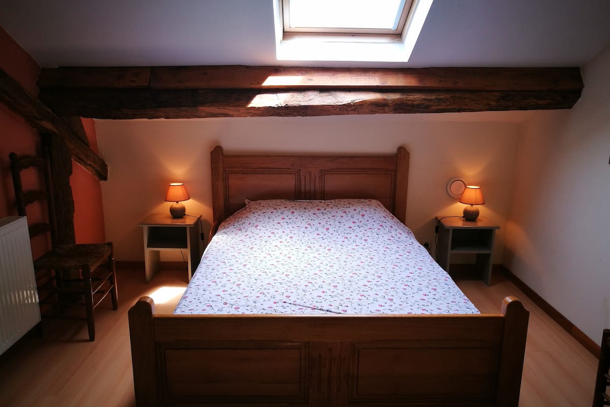 A bedroom with a wooden bed, two bedside tables with lamps, a radiator, and a skylight.