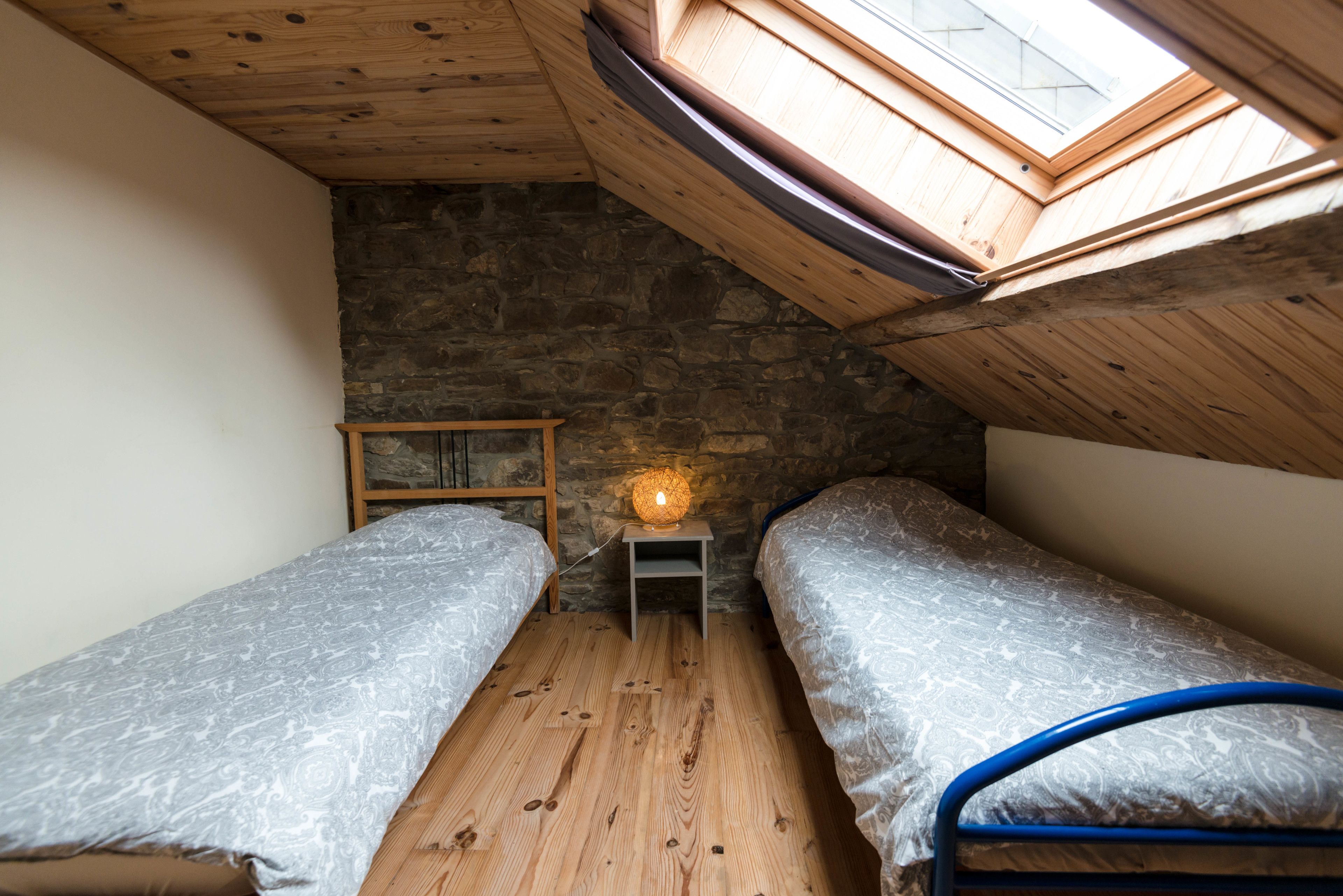 Een kleine, gezellige kamer met twee bedden, een stenen muur, houten balken en een dakraam.
