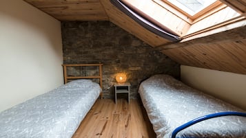 Een kleine, gezellige kamer met twee bedden, een stenen muur, houten balken en een dakraam.