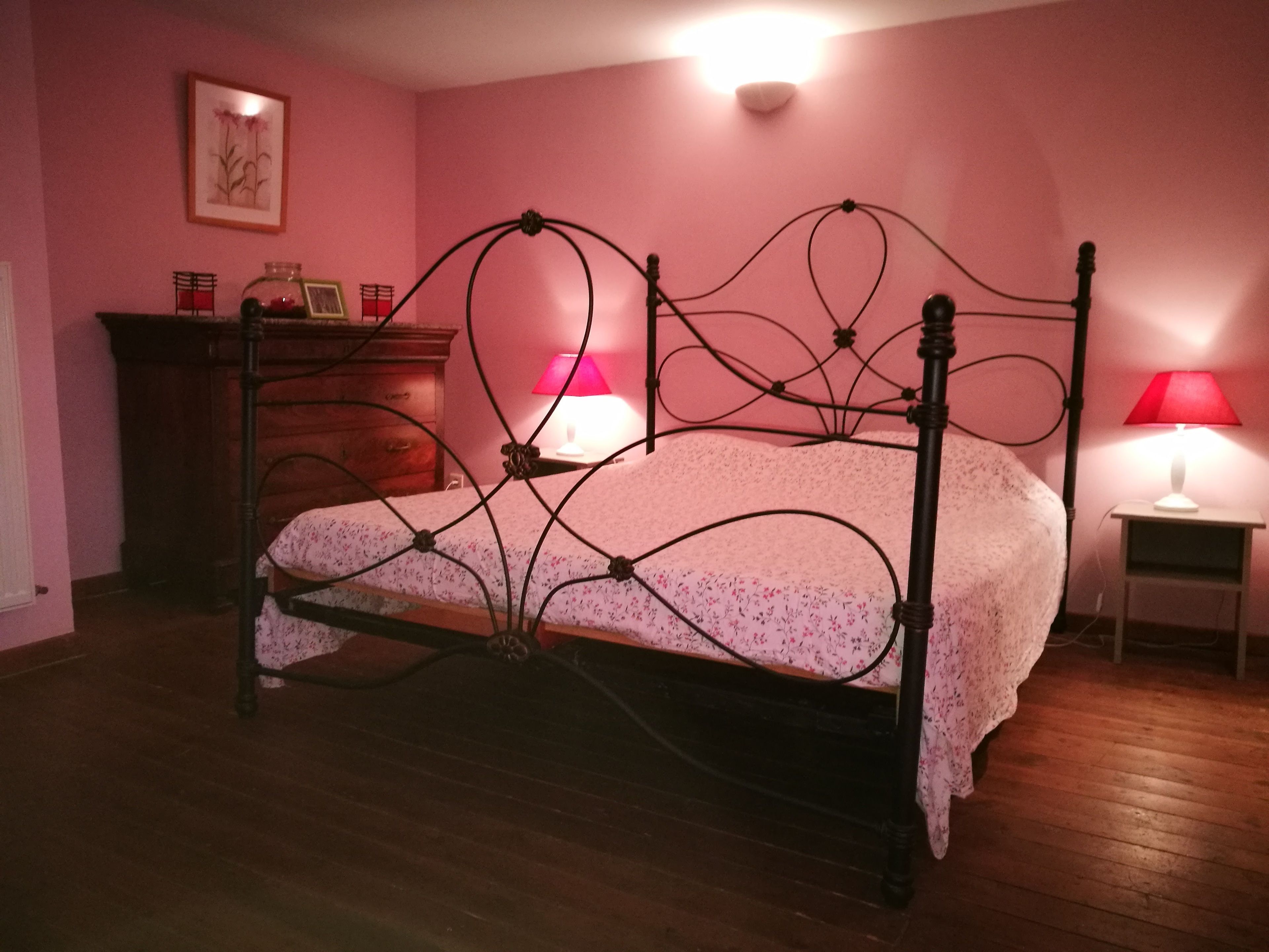 Ein Schlafzimmer mit einem Himmelbett, einer Holzkommode, zwei Nachttischlampen und einem gerahmten Bild an der Wand.