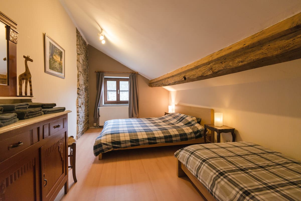 A bedroom with two beds, a dresser, a mirror, and a window with curtains.