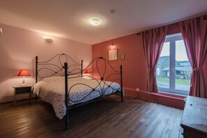 Un dormitorio con piso de madera, una cama con dosel, dos lámparas de noche, un ventanal con cortinas y vistas al exterior.